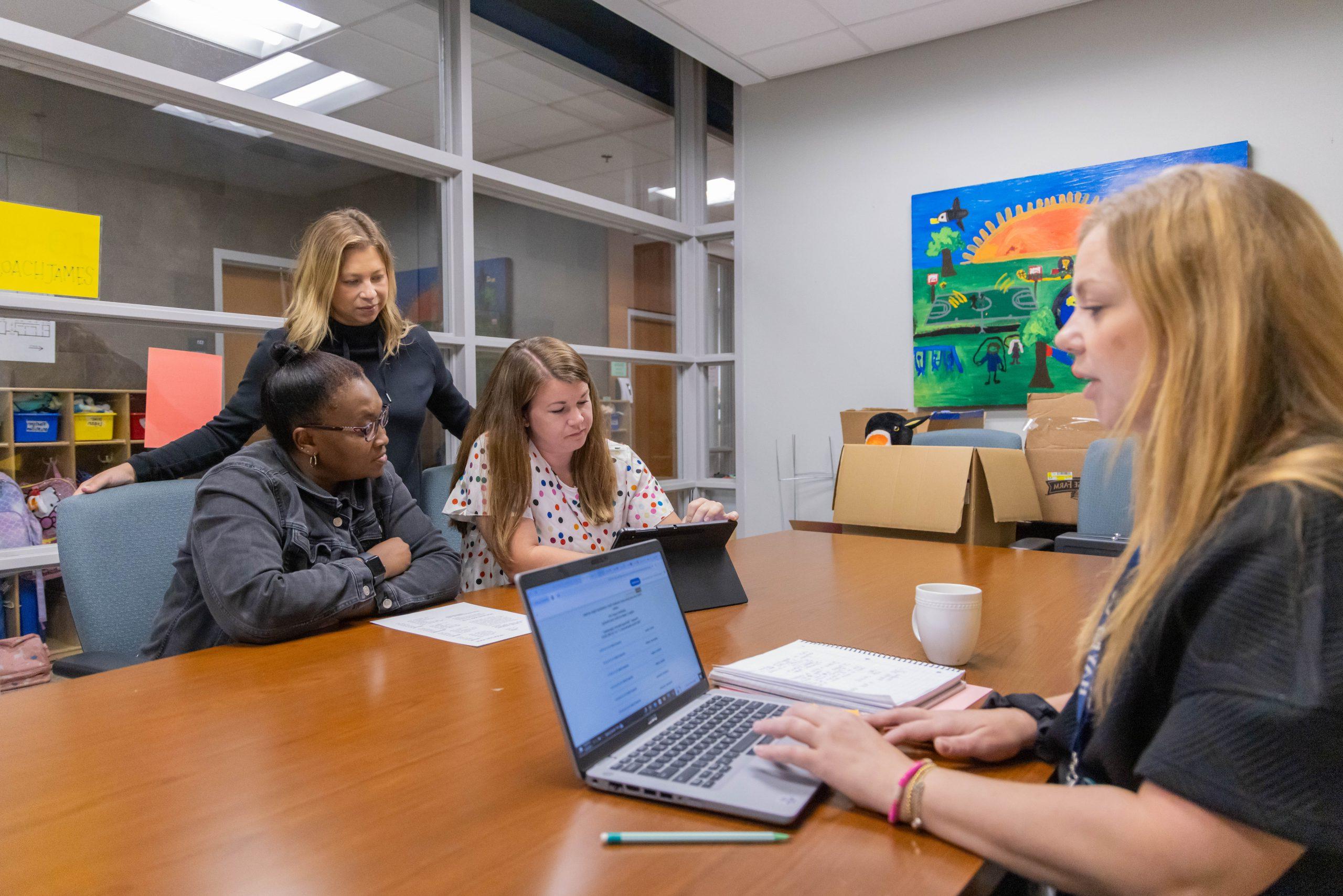 School administrators sitting around a conference table in a meeting, with a laptop and other materials on the table.